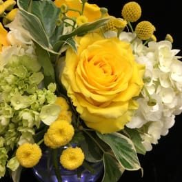 Yellow roses with white hydrangeas and round yellow blooms in a blue glass vase