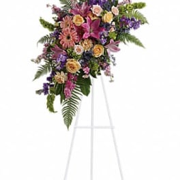 Standing spray of pink lilies, gerbera daisies, and roses with purple accents on a white easel