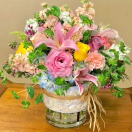 Mixed bouquet of pink, peach, yellow, and blue flowers in a glass vase