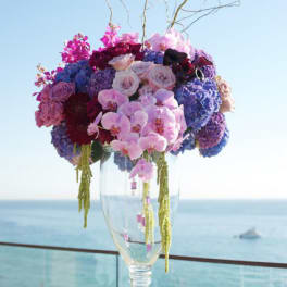 Tall floral arrangement in a clear glass vase with pink, purple, and blue blooms