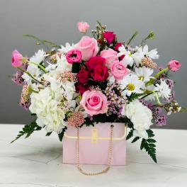 Pink and white flower arrangement in a pink gift box with a gold chain handle