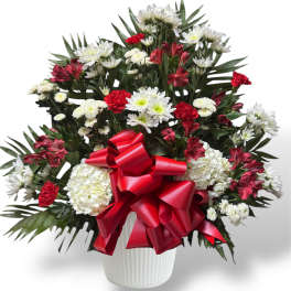 Red and white mixed flower arrangement in a white vase with a red bow