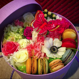 Round box of mixed roses, carnations, anemone, and macarons with a red butterfly topper