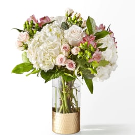 White and pink floral arrangement in a clear glass vase with a gold base