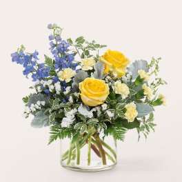 Yellow roses and blue delphinium in a clear glass vase
