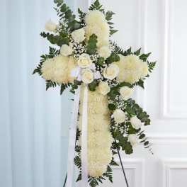 Tall white floral cross with roses and ribbon on a stand for a memorial display