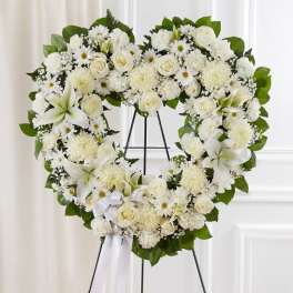 Heart-shaped white floral wreath with lilies and roses on a stand