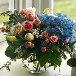Bouquet of pink and cream roses with blue hydrangeas in a glass vase