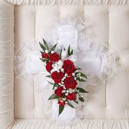 White fabric cross with red roses and white accent flowers inside a cream casket interior.