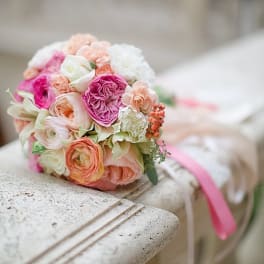 Round bouquet of pink, peach, and white flowers with a pink ribbon
