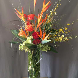 Tall tropical arrangement with orange birds of paradise and red roses in a glass vase