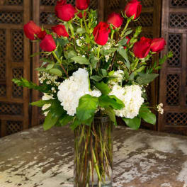 Red roses and white hydrangeas arranged in a clear glass vase.