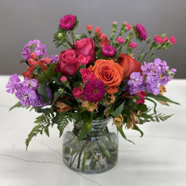 Mixed bouquet of pink, orange, and purple flowers in a clear glass vase