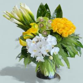 Bouquet of yellow roses, white orchids, and calla lilies in a glass vase