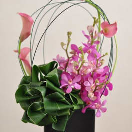 Pink calla lilies and orchids in a black vase with arched stems