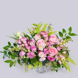 Low pink rose and ranunculus arrangement with snapdragons and bright green ferns in a clear glass vase