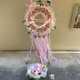 Pink and white floral standing wreath with ribbons and a "Peace and Prayers" sign