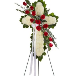 Standing cross of white flowers with red roses and white ribbon on a metal easel