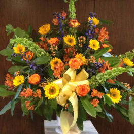 Large mixed bouquet with yellow sunflowers, orange roses, and a yellow ribbon in a vase