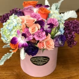 Mixed bouquet of roses, orchids, and hydrangeas in a pink hat box