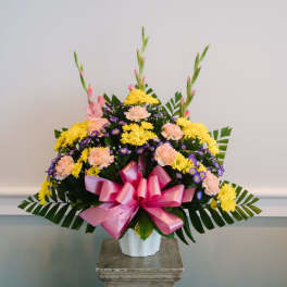 Colorful floral arrangement in a white vase with a pink bow