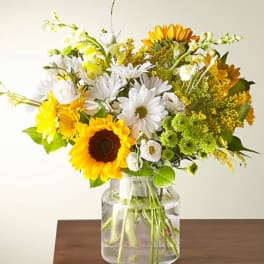 Bouquet of sunflowers, white daisies, and yellow flowers in a glass vase