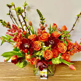 Orange roses and burgundy orchids in a clear glass vase