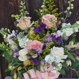 Pink and white roses with purple filler flowers in a white hatbox