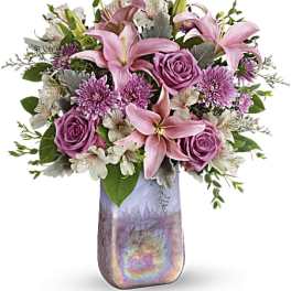 Pink lilies and roses arranged in a tall iridescent vase