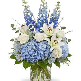 Blue hydrangeas, white lilies, and roses in a glass vase