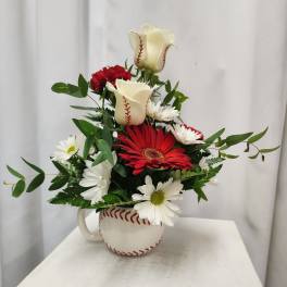 Red and white flowers arranged in a baseball-shaped mug