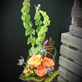 Tall floral arrangement with orange roses and green spikes in a rustic container