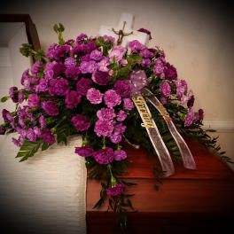 Purple carnation funeral spray with ribbons on a casket