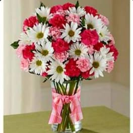 Bouquet of white daisies and pink carnations in a glass vase with a pink ribbon