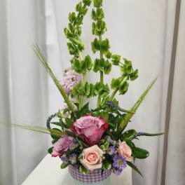 Tall floral arrangement with pink and lavender roses in a mint container