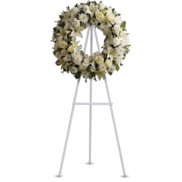 White funeral wreath of roses, lilies, and mums displayed on a tall white easel