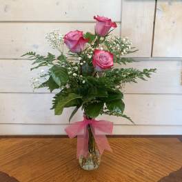 Pink roses in a clear glass vase with baby's breath and a pink ribbon
