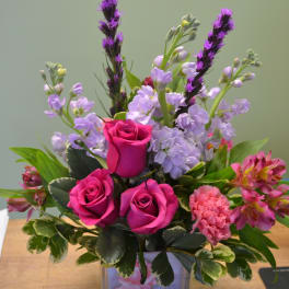 Pink roses and lavender flowers arranged in a clear square vase