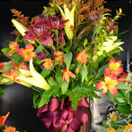 Tall bouquet of lilies, alstroemeria, and burgundy mums in a vase with a ribbon