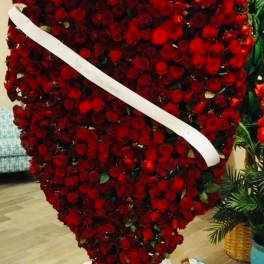 Heart-shaped arrangement of red roses with a white ribbon across it