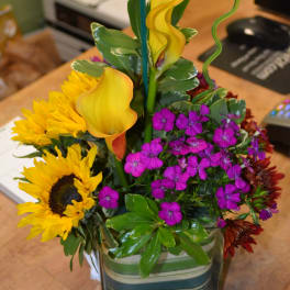 Mixed bouquet with sunflowers, yellow calla lilies, and purple dianthus in a glass vase