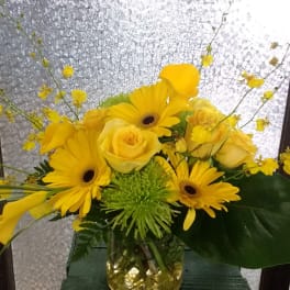 Yellow roses and gerbera daisies arranged in a glass vase