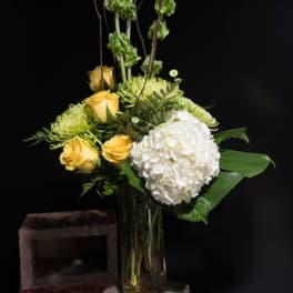 Yellow roses and a white hydrangea in a tall glass vase