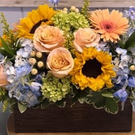 Mixed bouquet with sunflowers, peach roses, and blue hydrangeas in a wooden box
