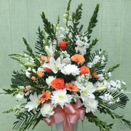 Standing floral spray with white lilies, orange roses, and white daisies