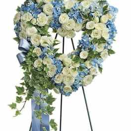Heart-shaped floral wreath with white roses and blue hydrangeas on an easel