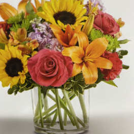 Mixed bouquet of sunflowers, roses, and lilies in a clear glass vase