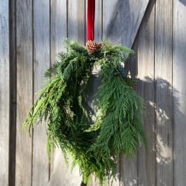 Evergreen wreath with a red ribbon and pinecone hanging on a wooden fence
