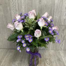 Bouquet of pale pink roses and purple daisies in a glass vase