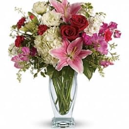 Tall glass vase of pink lilies, red roses, white hydrangeas, and mixed pink blooms